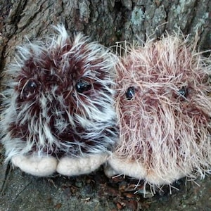 May include: Two brown and white fuzzy creatures with black eyes. They are sitting on a tree trunk.