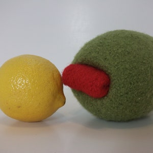 May include: A yellow lemon and a green felt olive with a red felt accent. The olive is slightly larger than the lemon.
