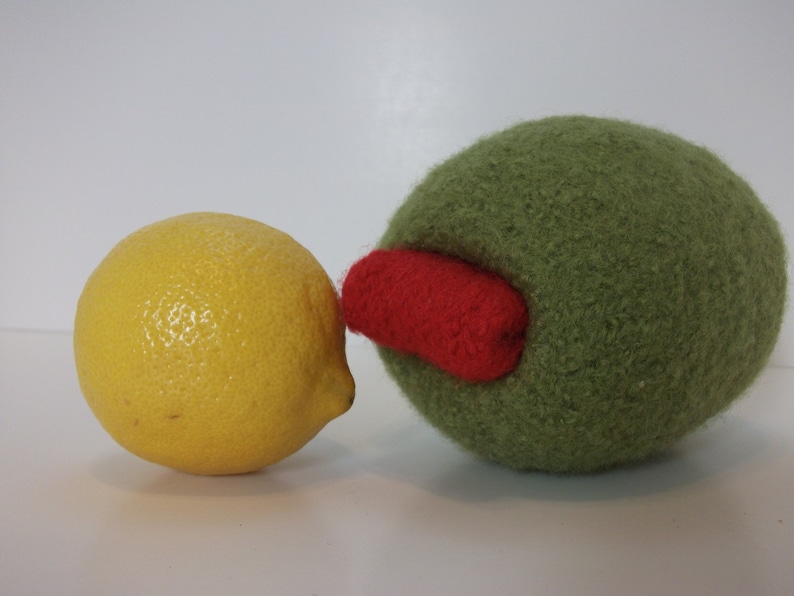 May include: A yellow lemon and a green felt olive with a red felt accent. The olive is slightly larger than the lemon.