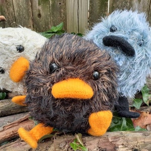 Peut inclure: Trois jouets en peluche en forme d'oiseaux. L'oiseau &agrave; gauche est blanc avec des yeux noirs et un bec orange. L'oiseau au centre est noir avec des plumes brunes, un bec orange et des yeux noirs. L'oiseau &agrave; droite est bleu avec des yeux noirs et un bec noir.