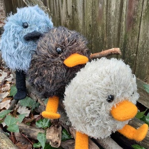Peut inclure: Trois jouets en peluche moelleux faits &agrave; la main ressemblant &agrave; des oiseaux. Le premier est bleu avec des pattes noires, le second est brun avec des pattes orange et le troisi&egrave;me est blanc avec des pattes orange.