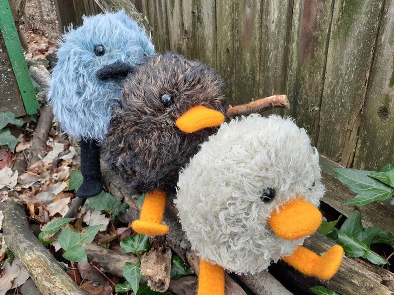 Peut inclure: Trois jouets en peluche moelleux faits &agrave; la main ressemblant &agrave; des oiseaux. Le premier est bleu avec des pattes noires, le second est brun avec des pattes orange et le troisi&egrave;me est blanc avec des pattes orange.