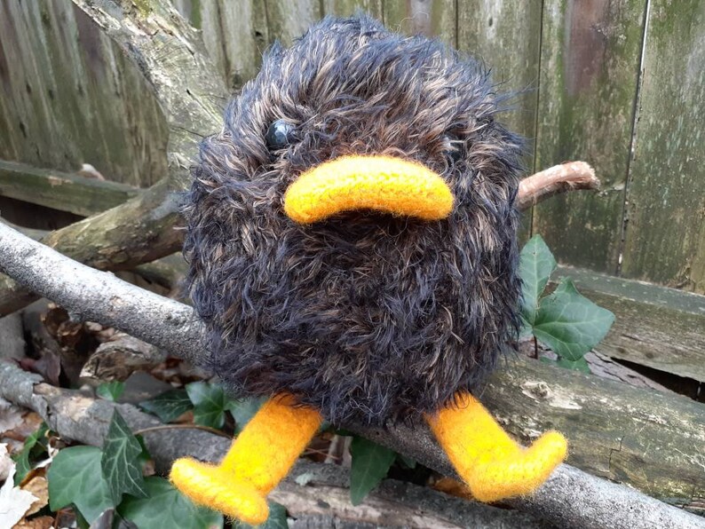 Peut inclure: Un animal en peluche noir et brun avec un bec et des pattes jaunes. L'animal est assis sur une branche.