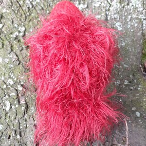 May include: A vibrant red, fluffy object with a dense, textured appearance. The object is composed of numerous fine, hair-like strands, creating a soft, cloud-like form. The color is a bright, saturated red.