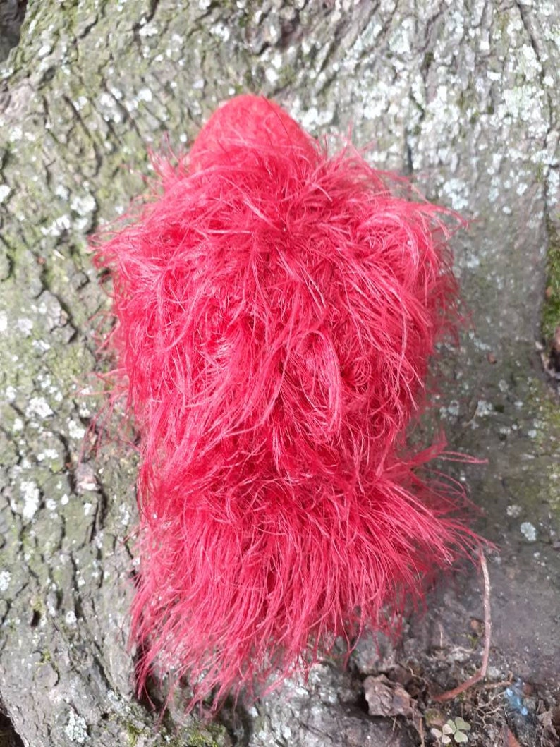 May include: A vibrant red, fluffy object with a dense, textured appearance. The object is composed of numerous fine, hair-like strands, creating a soft, cloud-like form. The color is a bright, saturated red.