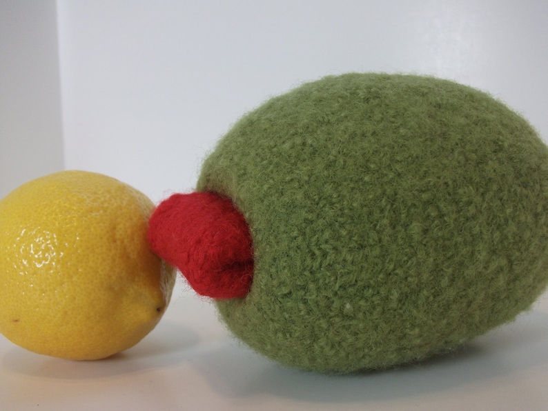 May include: A green felt ball with a red felt patch on the side, next to a yellow lemon.