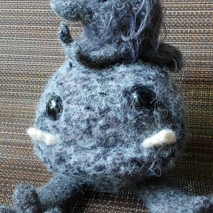 May include: A handmade gray plush creature with large black eyes, white tusks, and small arms and legs. A smaller creature sits on top of the larger one. The plush toy is made of a fuzzy material.