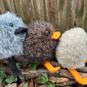 Peut inclure: Trois jouets d'oiseaux en peluche faits &agrave; la main avec des plumes de diff&eacute;rentes couleurs et des becs orange. Les oiseaux sont assis sur une branche.