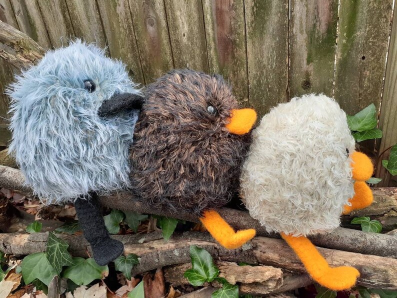 Peut inclure: Trois jouets d'oiseaux en peluche faits &agrave; la main avec des plumes de diff&eacute;rentes couleurs et des becs orange. Les oiseaux sont assis sur une branche.