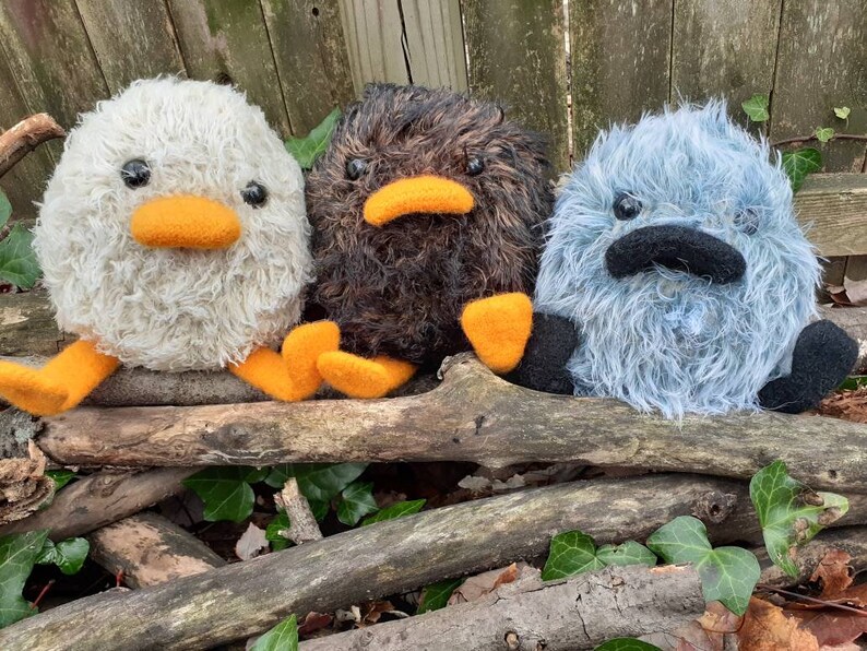 Peut inclure: Trois peluches, un canard blanc, un oiseau brun et une cr&eacute;ature bleue et duveteuse, sont assis sur un tas de branches. Les jouets ont des becs et des pieds orange.