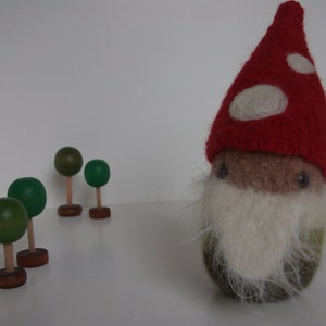 May include: A felt gnome with a red hat and white polka dots, a white beard, and a green body. The gnome is standing in front of four small wooden trees with green tops.