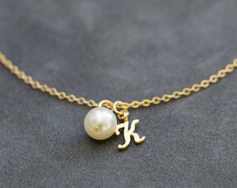May include: A gold chain necklace with a single pearl and a gold letter K charm.
