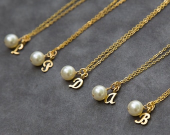 May include: Five gold-toned necklaces, each featuring a delicate chain, a single round white pearl bead, and a gold-toned metal letter charm. The letters displayed on the charms are L, P, D, a, and B, arranged in a diagonal line across the frame.