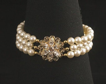 May include: A triple strand pearl bracelet with a gold and crystal flower accent.