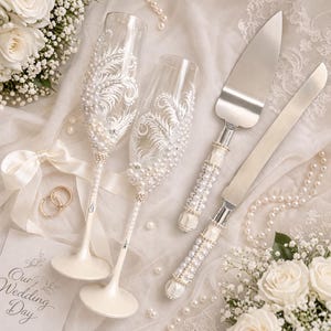 pearl wedding glasses, champagne flutes with pearls, engraved wedding glasses, bride and groom toasting flutes, pearl cake server and knife set, coastal beach wedding accessories, elegant bridal table details, luxury wedding flutes, wedding cake cutting set, ivory lace background, romantic wedding styling, handmade wedding glasses, pearl handle cake server, wedding reception essentials, bride groom glasses set, beach wedding decor, classic wedding accessories