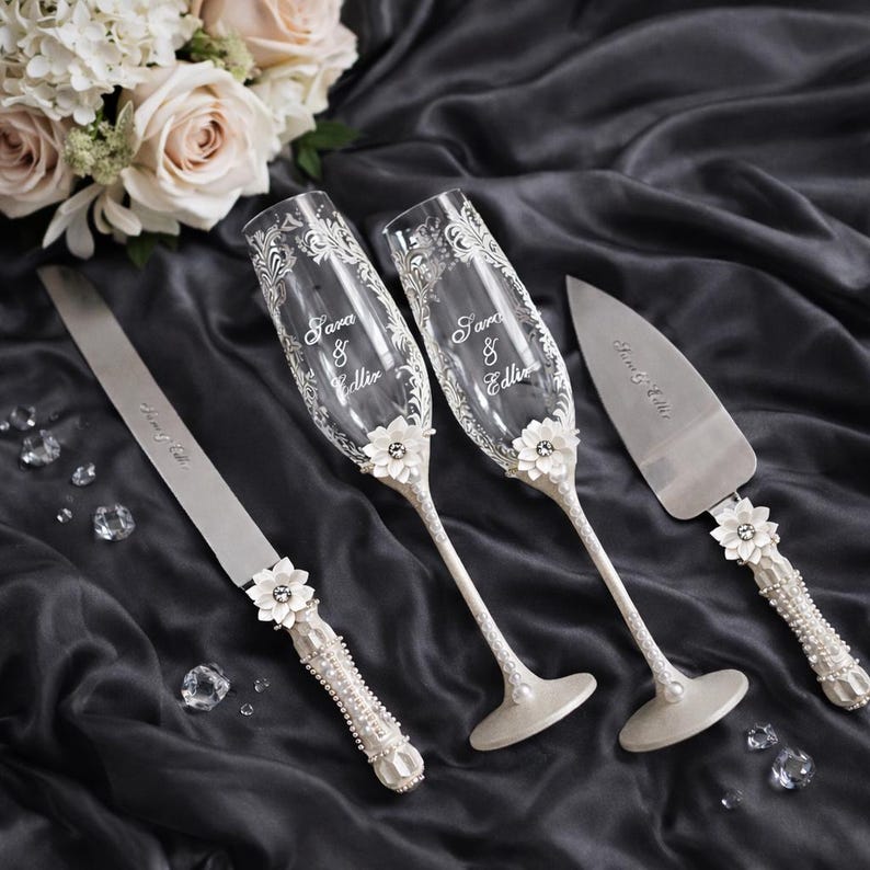 Personalized white wedding toasting set with 3D flowers, engraved champagne flutes, white wedding glasses, floral wedding glass set, sculpted flower decor glasses, custom wedding flutes with names, elegant white wedding accessories, cake knife and server white set, floral handled wedding knife server, romantic wedding toast glasses, bride groom toasting flutes, custom wedding glassware, white floral wedding decor, handmade wedding toasting set, wedding reception accessories white