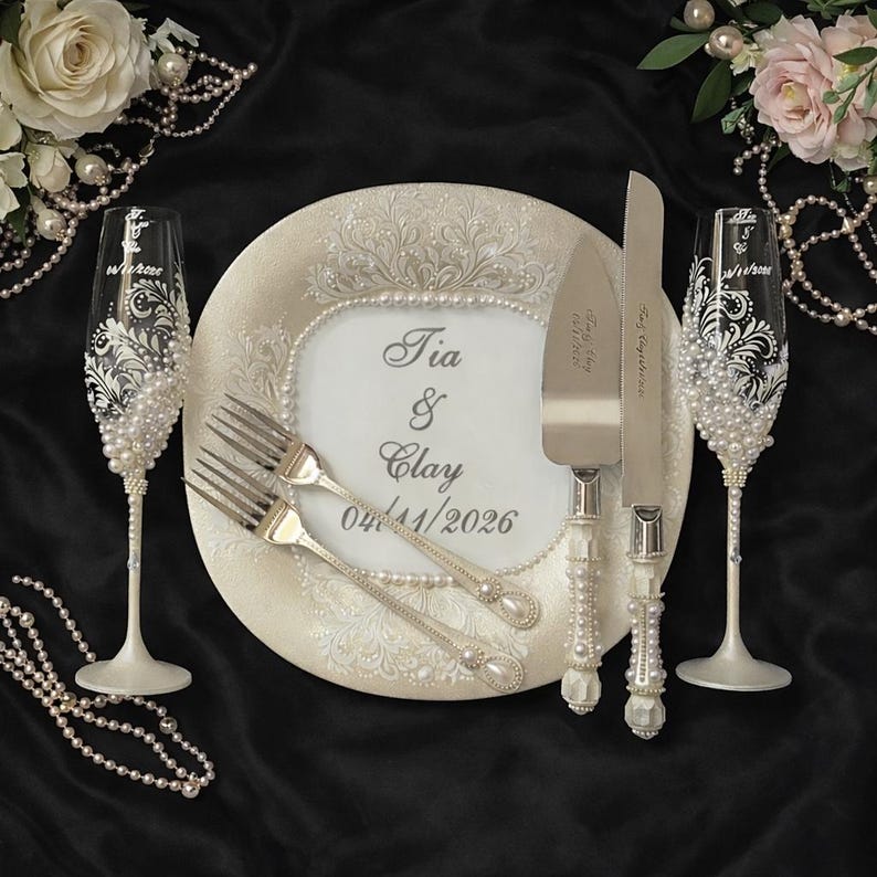 Peut inclure: Ensemble de service &agrave; g&acirc;teau de mariage ivoire avec fl&ucirc;tes &agrave; champagne, assiette, fourchettes, couteau et serveur &agrave; g&acirc;teau. L'ensemble pr&eacute;sente des perles et les noms "Tia & Clay" et la date "04/11/2026".