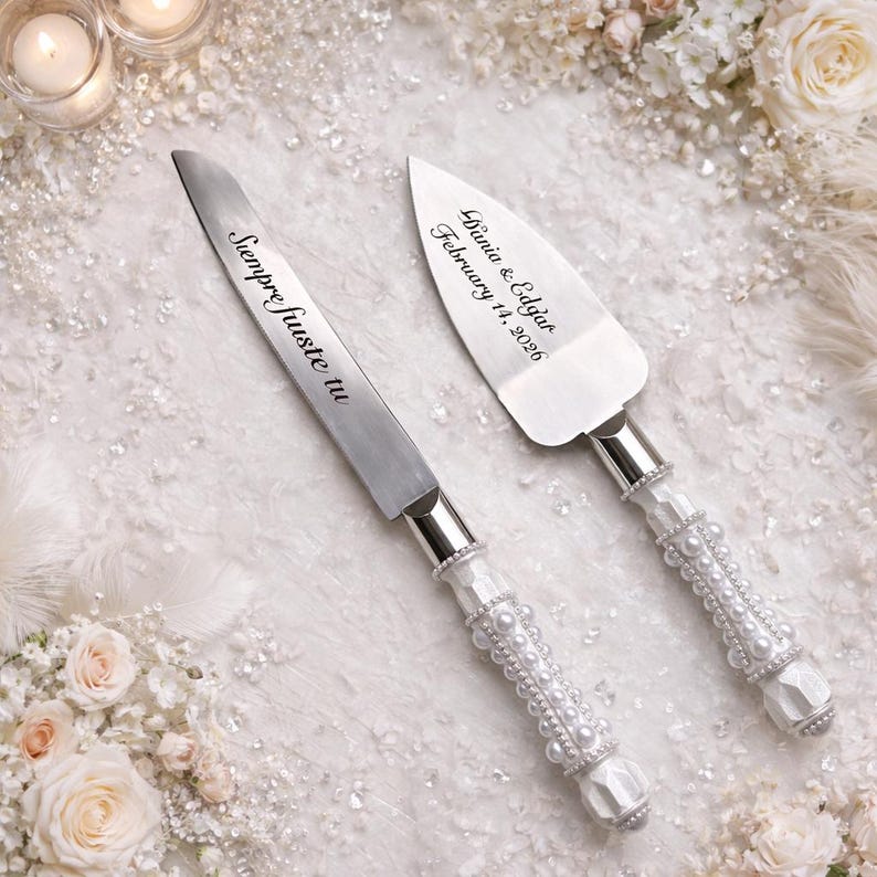 May include: A silver cake knife and server set with handles decorated in white pearls. The knife blade is engraved with the text "Siempre Juste tu" and the server blade is engraved with the text "Dunia & Edgar February 14, 2026".