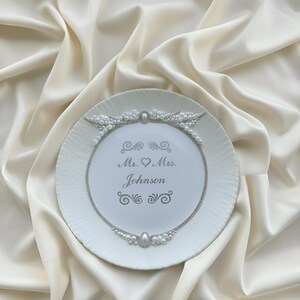May include: White decorative plate with a textured rim, adorned with a pearl and silver chain design. The plate features the inscription "Mr. & Mrs. Johnson" in elegant script, perfect for weddings or anniversaries.