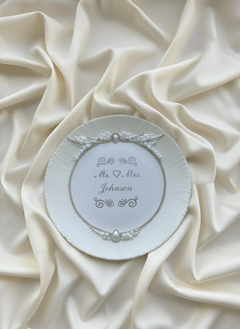 May include: White decorative plate with a textured rim, adorned with a pearl and silver chain design. The plate features the inscription "Mr. & Mrs. Johnson" in elegant script, perfect for weddings or anniversaries.