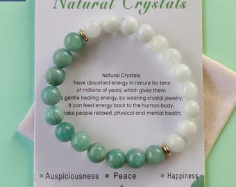 Puede incluir: Un brazalete con cuentas de Amazonita y Piedra Lunar Azul. Las cuentas alternan entre blanco y verde azulado, separadas por espaciadores dorados. El brazalete se muestra en una tarjeta con el texto "Natural Crystals" y "Celestial Duo - Amazonite & Blue Moonston".