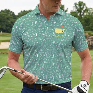 Op de afbeelding: Groen golfpoloshirt met een wit patroon van golfgerelateerde iconen. Het shirt heeft een gele kaart met een rode vlag en de naam "JAMES". De persoon draagt een zwarte pet, een blauwe broek en een witte golfhandschoen en houdt een golfclub vast.