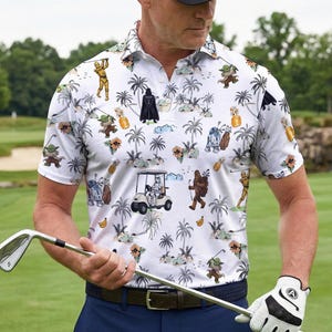 Pu&ograve; includere: Polo da golf bianco con una stampa tropicale a tema Star Wars con personaggi come Darth Vader, Yoda e R2-D2. La camicia ha un colletto e maniche corte. La persona indossa un berretto nero, pantaloni blu e un guanto da golf bianco.