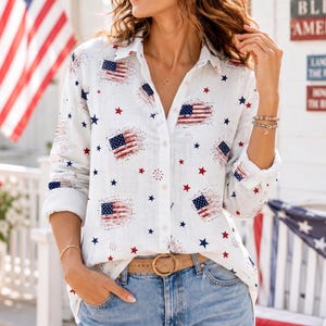 May include: White button-down shirt with a patriotic American flag and star pattern. The shirt features red, white, and blue accents, a collared neckline, and long sleeves. The model is wearing blue jeans and a brown belt.