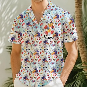 Może przedstawiać: Biała koszula z krótkim rękawem zapinana na guziki z kolorowym nadrukiem przedstawiającym postacie z kreskówek, łodzie i symbole marynistyczne. Koszula ma kołnierzyk i kieszeń po lewej stronie. Na koszuli nadrukowany jest tekst "Name".