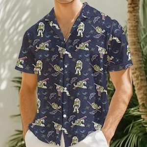 Puede incluir: Una camisa de botones de manga corta azul marino con un patrón repetido de Buzz Lightyear de Toy Story. El patrón incluye estrellas, planetas y murciélagos.