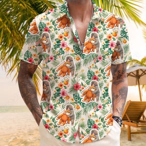 Può includere: Camicia a maniche corte con bottoni e motivo floreale tropicale. La camicia presenta un motivo ripetuto di scimmie che si abbracciano, insieme a fiori e fogliame nei toni dell'arancione, del rosa e del verde. Lo sfondo è color crema chiaro.
