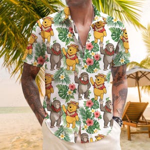 Può includere: Camicia bianca a maniche corte con un motivo tropicale con orsi e scimmie dei cartoni animati. Il design include foglie verdi, fiori rosa e i personaggi indossano collane di fiori e cappelli. La camicia ha una vestibilità ampia.