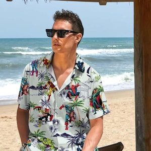 以下が含まれることがあります： 白のボタンダウンシャツと、さまざまなマーベルのスーパーヒーローが描かれたトロピカルプリントのマッチングショーツ。シャツは襟付きで半袖。ショーツはゴムウエストバンドとドローストリング付きです。