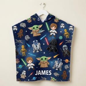 May include: A dark blue hooded towel featuring a repeating pattern of Star Wars characters including Grogu, Luke Skywalker, Darth Vader, R2-D2, C-3PO, Chewbacca, and Stormtroopers, along with spaceships and planets. The name JAMES is printed in white.