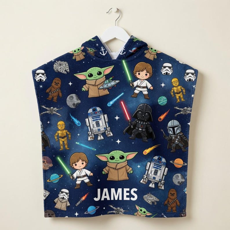 May include: A dark blue hooded towel featuring a repeating pattern of Star Wars characters including Grogu, Luke Skywalker, Darth Vader, R2-D2, C-3PO, Chewbacca, and Stormtroopers, along with spaceships and planets. The name JAMES is printed in white.