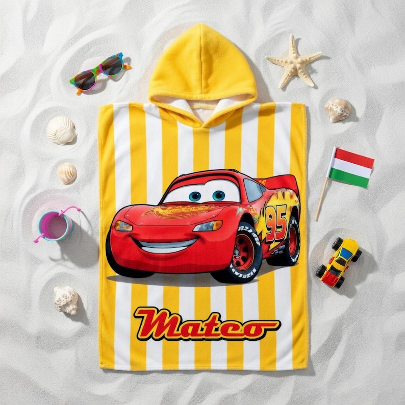 K&ouml;nnte beinhalten: Ein gelb-wei&szlig; gestreiftes Kapuzen-Badetuch mit einem roten Cartoon-Rennwagen mit der Nummer 95. Auf dem Handtuch ist der Name "Mateo" aufgedruckt. Zus&auml;tzliche Strandaccessoires sind Sonnenbrillen, Muscheln und ein Spielzeugauto.