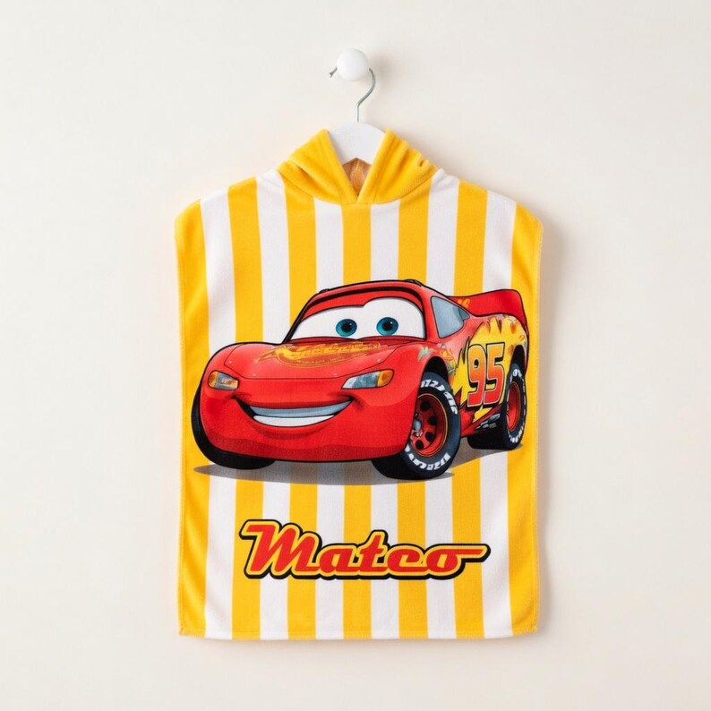K&ouml;nnte beinhalten: Ein Kapuzen-Badetuch mit einem roten Lightning McQueen-Rennwagen-Motiv aus dem Film Cars. Das Handtuch hat gelbe und wei&szlig;e vertikale Streifen und den Namen "Mateo" in gelber Schrift. Das Handtuch h&auml;ngt an einem wei&szlig;en Haken.