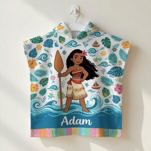 K&ouml;nnte beinhalten: Ein wei&szlig;es Strandtuch mit Kapuze und einer Cartoon-Illustration einer polynesischen Prinzessin, die ein Paddel h&auml;lt. Das Handtuch ist mit tropischen Blumen, Bl&auml;ttern und Meereswellen verziert. Der Name "Adam" ist unten aufgedruckt.
