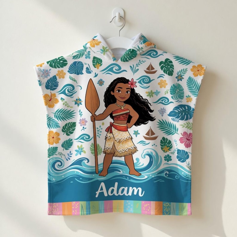 K&ouml;nnte beinhalten: Ein wei&szlig;es Strandtuch mit Kapuze und einer Cartoon-Illustration einer polynesischen Prinzessin, die ein Paddel h&auml;lt. Das Handtuch ist mit tropischen Blumen, Bl&auml;ttern und Meereswellen verziert. Der Name "Adam" ist unten aufgedruckt.