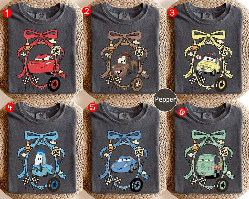 May include: Six charcoal gray t-shirts with different cartoon car designs inside decorative frames. Each frame has a bow, Route 95 sign, and a tire. The designs include a red car, a brown truck, a yellow car, a blue car, and a green van.