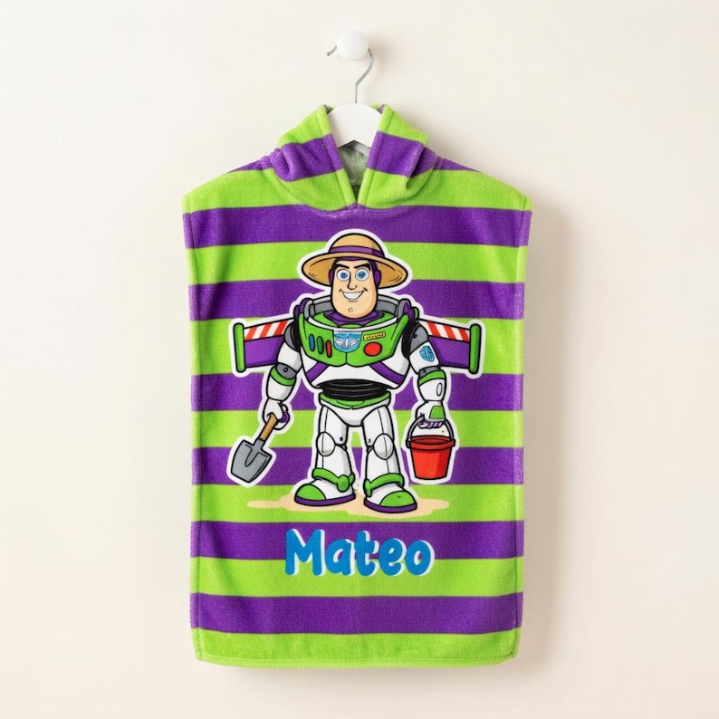 May include: A hooded beach towel with green and purple horizontal stripes. The towel features a cartoon image of Buzz Lightyear holding a shovel and a red bucket. The name "Mateo" is written in blue script below the character.