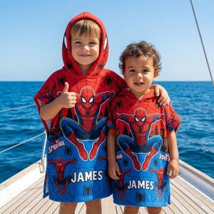 May include: Two red and blue hooded poncho towels featuring a Spider-Man graphic print, a spider web pattern, and the name James printed in white block letters. The towels have a hood and a loose, sleeveless fit for easy wear after swimming.