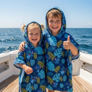 Puede incluir: Dos toallas tipo poncho con capucha que presentan un fondo azul oscuro con un patr&oacute;n repetitivo del personaje Stitch y hojas tropicales en tonos azul claro, turquesa y amarillo. Las prendas tienen mangas cortas y capucha integrada.
