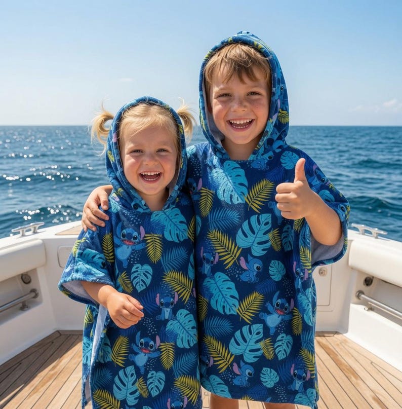 Puede incluir: Dos toallas tipo poncho con capucha que presentan un fondo azul oscuro con un patr&oacute;n repetitivo del personaje Stitch y hojas tropicales en tonos azul claro, turquesa y amarillo. Las prendas tienen mangas cortas y capucha integrada.