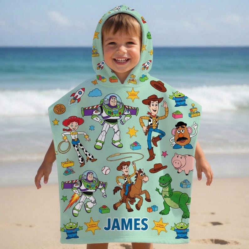 May include: A light green hooded towel featuring a repeating pattern of Toy Story characters including Buzz Lightyear, Woody, Jessie, Mr. Potato Head, Rex, and Bullseye. The name JAMES is printed in blue capital letters at the bottom center.