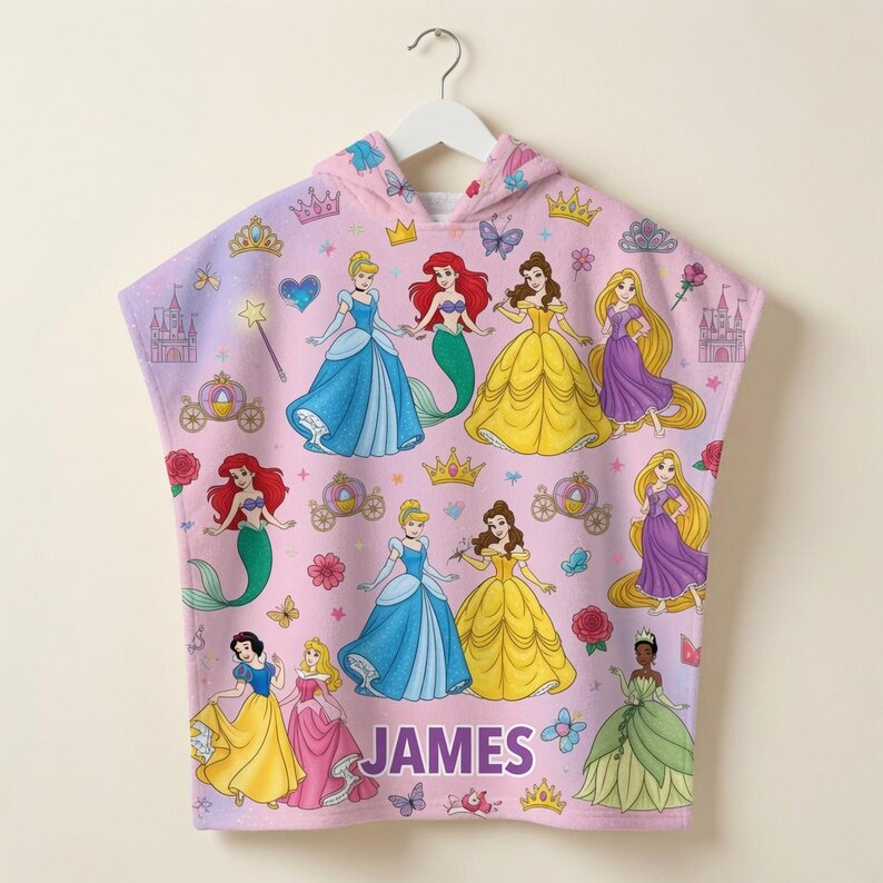 Puede incluir: Una toalla con capucha rosa con un patr&oacute;n repetitivo de varias princesas Disney, incluyendo a Cenicienta, Ariel, Bella, Rapunzel, Blancanieves y Tiana. El dise&ntilde;o incluye coronas, castillos, carruajes y flores. El nombre JAMES est&aacute; impreso en morado.