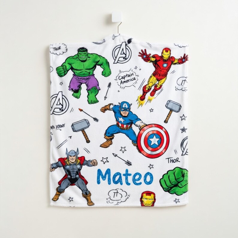 May include: White superhero-themed blanket featuring illustrations of Hulk, Iron Man, Captain America, and Thor. The blanket includes the name "Mateo" in blue, along with comic book style elements.