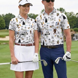 Pu&ograve; includere: Una coppia indossa camicie da golf abbinate con una stampa a tema Star Wars. Le camicie sono bianche con un motivo di palme e personaggi di Star Wars. La donna indossa una gonna a pieghe bianca e una visiera. L'uomo indossa pantaloni blu.