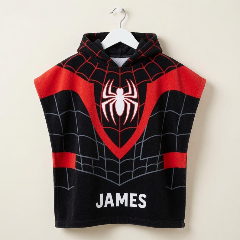 May include: A black hooded poncho towel featuring a red and black spiderweb pattern across the chest and shoulders. A large white spider emblem is centered on the chest, and the name JAMES is printed in white capital letters at the bottom hem.