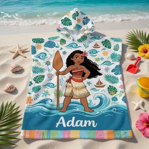 K&ouml;nnte beinhalten: Ein Strandtuch mit Kapuze mit einer Cartoon-Illustration einer polynesischen Frau, die einen Speer h&auml;lt. Das Handtuch hat einen wei&szlig;en Hintergrund mit blauen Wellen, Booten und floralen Mustern. Der Name "Adam" ist unten aufgedruckt.